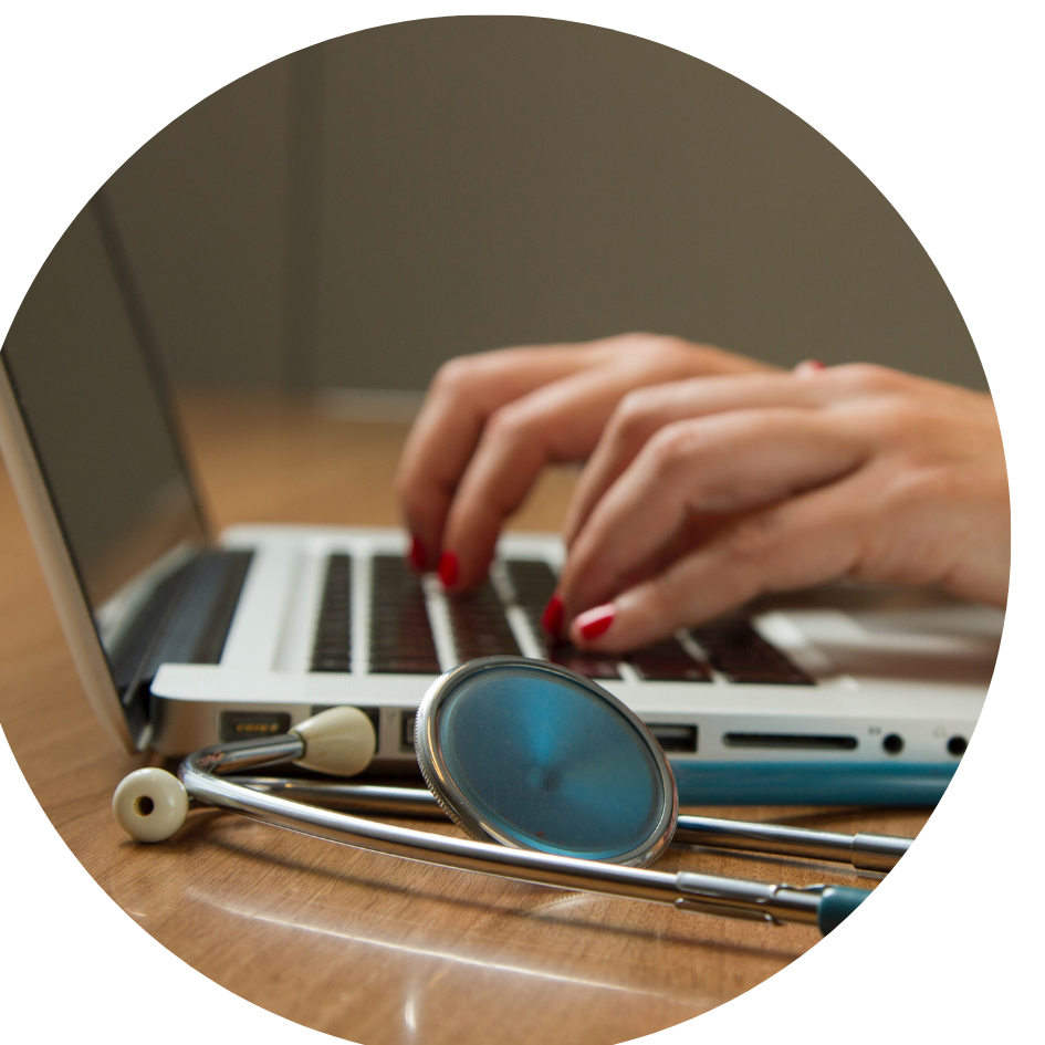 A person typing on a laptop with a stethoscope placed beside it
